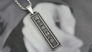 Macro detail of silver titanium steel pendant featuring six-syllable mantra engraving