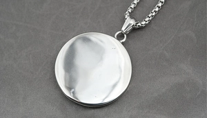 Detail of silver round pendant on box chain over grey textured fabric background