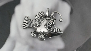 Macro detail of anglerfish pendant showing retro silver texture and sharp teeth