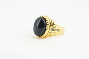 Détail d'une bague dorée avec une grande pierre noire ovale et petits zircons sur le côté
