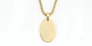 Detailed view of golden oval pendant with prayer hands and Spanish scripture engraving