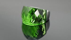 Macro shot of large faceted green emerald-style gemstone ring with silver metal band