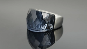 Macro shot of oversized grey multifaceted crystal ring on a dark reflective surface