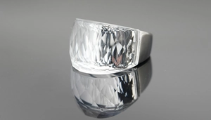 Detailed view of faceted crystal ring with polished wide band reflecting on a dark surface