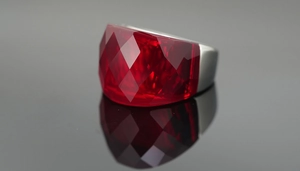 Macro shot of oversized ring featuring a ruby-red faceted gemstone on a matte silver band