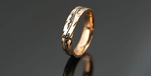Macro view of rose gold titanium ring with black tribal engraving and hammered edges