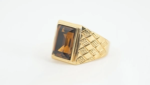 Detailansicht eines goldfarbenen Titanrings mit braunem Edelstein und gravierten Seitenmustern