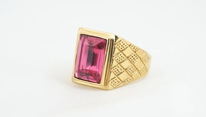 Details eines rosafarbenen Edelsteinrings mit goldener Schachbrett-Textur am Band