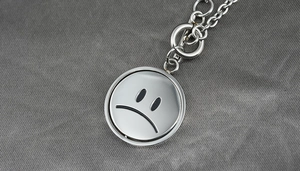 Close-up of a silver titanium steel spinning necklace with a sad face emoji pendant