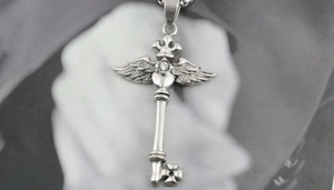 Détail d'un pendentif clé en argent avec ailes de couronne cœur cristal et croix
