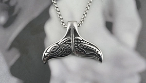 Macro detail of silver whale tail pendant with tribal carvings on a steel box chain