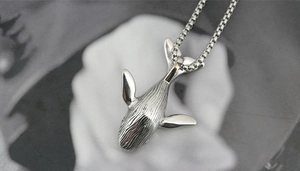 Macro detail of high-polished titanium steel whale pendant with intricate textured patterns