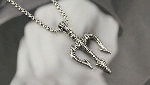 Vue macro du pendentif trident en acier titane avec volutes et gravures de crâne