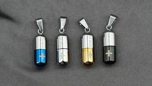 Gros plan de pendentifs gélules en quatre couleurs avec croix gravée sur acier poli