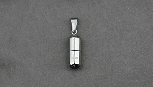 Macro d'un pendentif capsule argenté avec gravure Be Loved et croix sur tissu