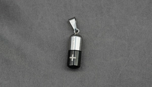 Détail d'un pendentif capsule en acier bicolore avec symbole de croix et gravure De Mood