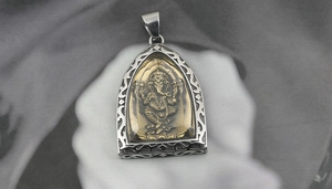 Detailed view of silver-tone Ganesh pendant with golden embossed relief and filigree frame