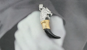 Detail of dragon head wolf tooth pendant in silver and gold tone titanium steel