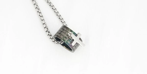 Macro detail of stainless steel cross and ring pendant with engraved Spanish scripture