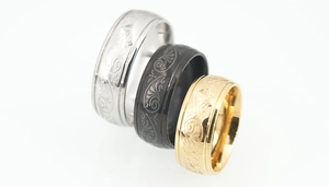 Detailed macro view of engraved floral patterns on silver, black, and gold steel rings