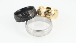 Detail of three stainless steel rings in black, gold, and silver with engraved vine patterns