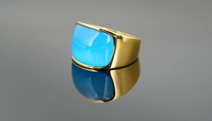 Makroaufnahme eines blauen Edelsteins auf breitem Goldring mit Spiegelreflexionen