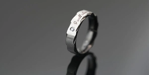 Detailansicht eines Titanstahlrings mit Wellenkanten, Gravur und kleinem Diamanten