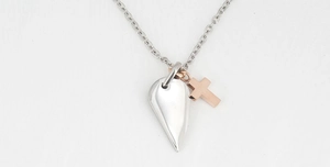 Close-up of a two-tone cross and heart wing pendant necklace in polished steel