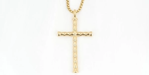Détail d'un pendentif croix dorée avec motif géométrique de losanges et fine chaîne