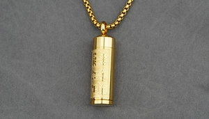 Macro detail of golden cylindrical sutra pendant necklace with engraved religious symbols