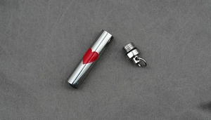 Detailed macro view of silver cylinder urn necklace with red heart and sealing ring