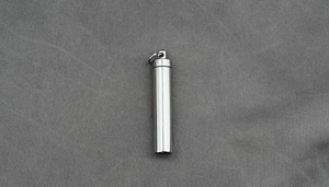 Macro view of a cylindrical stainless steel perfume urn pendant on grey fabric