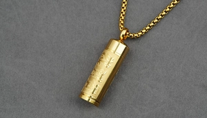 Detailed close-up of golden cylindrical Buddhist pendant with engraved scripture characters