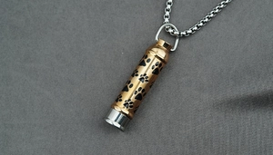 Détail du pendentif cylindrique doré avec empreintes de pattes sur une chaîne
