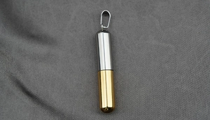 Detalle macro de un colgante de cápsula bicolor oro y plata con acabado de acero pulido