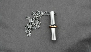Close-up of a silver and rose gold cylinder pendant on a sleek titanium steel chain
