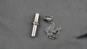 Macro shot of silver cylinder pendant with tricolor trinity rings and screw top closure