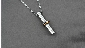 Detailed macro view of a silver cylinder ash pendant with interlocking gold and silver rings
