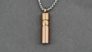 Detail of rose gold cylindrical memorial pendant with a silver box chain on grey fabric