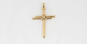 Macro detail of golden nail-shaped cross pendant showing industrial metallic texture