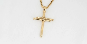 Macro shot of gold cross pendant made from crossed nails with a box chain necklace