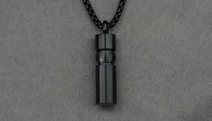 Macro shot of black brushed titanium steel cylindrical urn pendant on a matching box chain