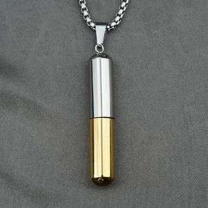 Collar con colgante de cápsula en acero inoxidable oro y plata sobre tela gris