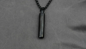 Close-up of a matte black titanium steel cylinder capsule pendant on a square link chain