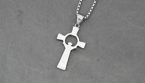 Macro detail of silver cross pendant with hollow center and box chain on grey fabric