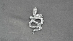 Macro detail of silver winding snake pendant with full crystal pavé on textured background