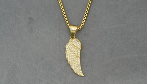 Macro shot of gold angel wing pendant necklace with pavé crystal settings on grey fabric