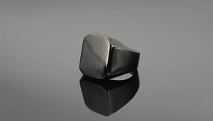 Vue macro d'une bague chevalière carrée noire polie avec reflet sur fond sombre