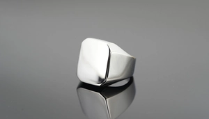 Gros plan d'une bague chevalière carrée en argent poli avec reflets sur miroir sombre