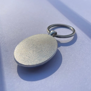 Silver oval metal firefighter keychain with textured back and polished front on white surface